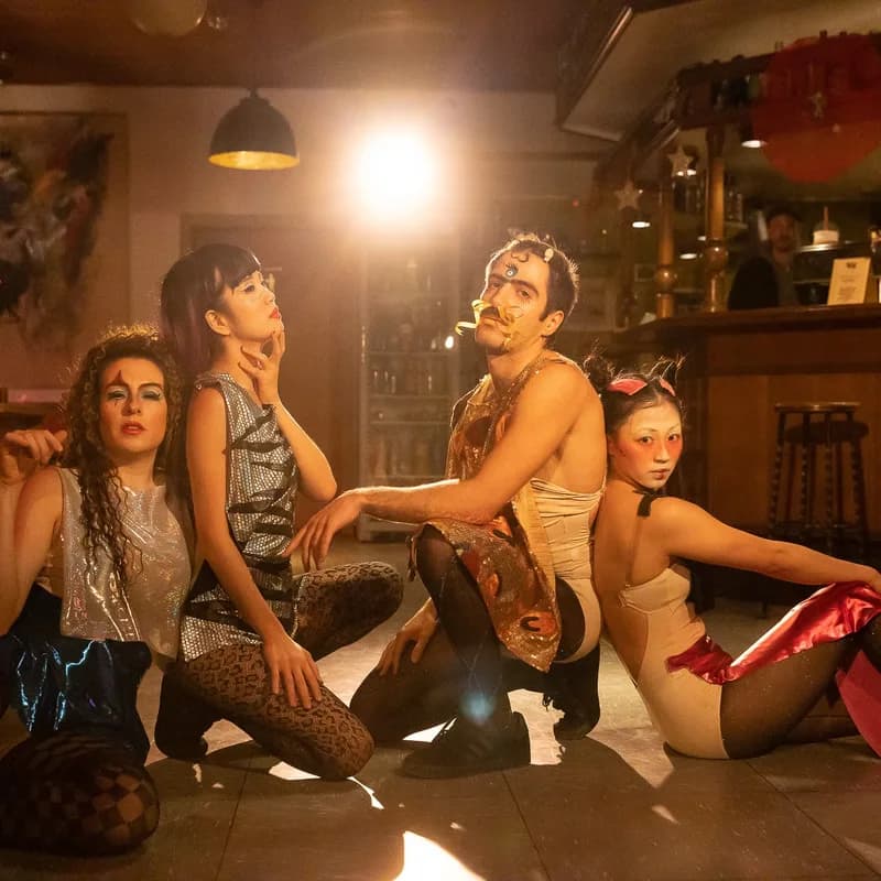 4 Personen im Drag-Style posieren im Gegenlicht eines Scheinwerfers.