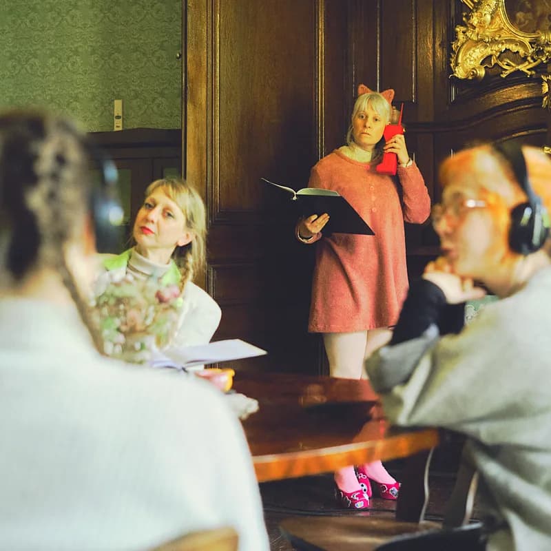 4 Personen an einem Tisch, teils mit Kopfhöhrern lesen einen Text.