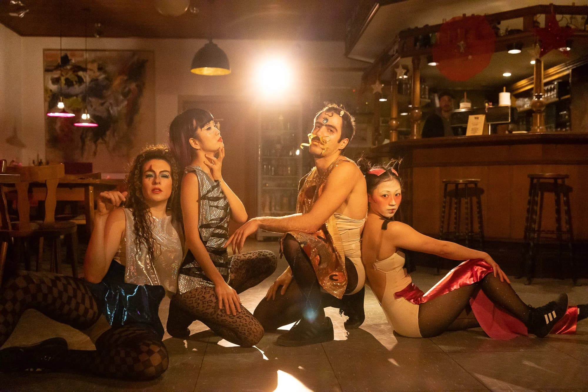 4 Personen im Drag-Style posieren im Gegenlicht eines Scheinwerfers.