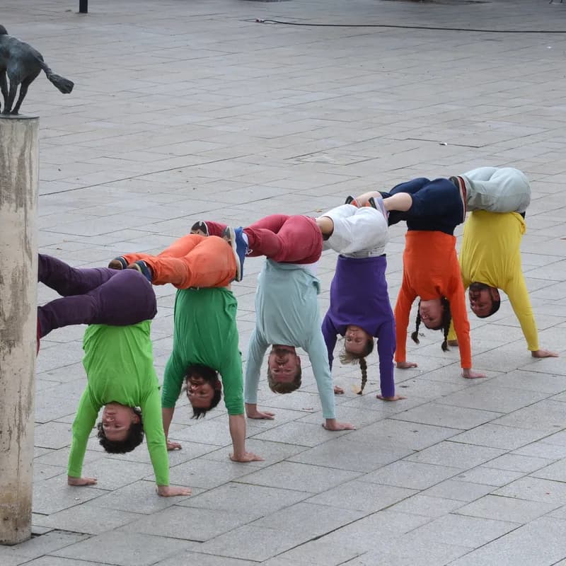 6 bunt gekleidete Personen im Handstand hintereinander.