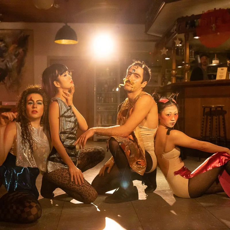4 Personen im Drag-Style posieren im Gegenlicht eines Scheinwerfers.